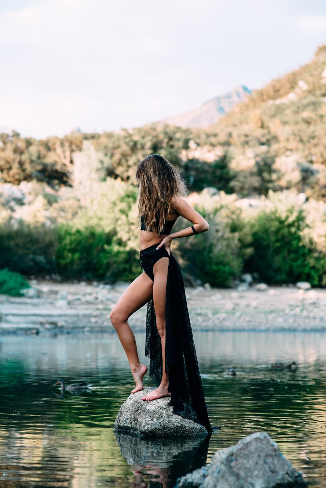 a girl wearing Valencia's black outfit standing on a rock in the middle of a lake